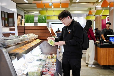 Student browsing fresh packaged meals and salads in a University of Waterloo campus dining area.
