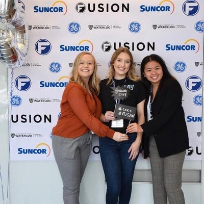 Three females standing in front of Fusion confrence banner