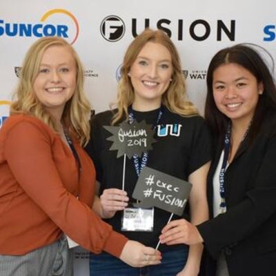 Three females standing in front of Fusion confrence banner