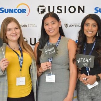 Three females standing in front of Fusion confrence banner