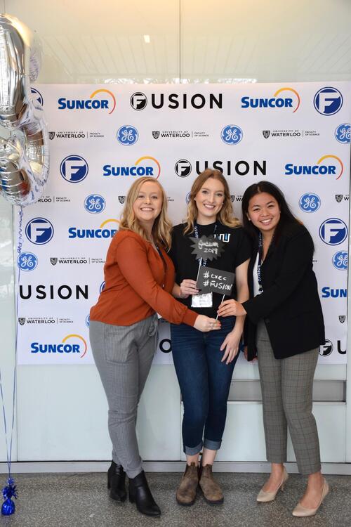 Three females standing in front of Fusion confrence banner