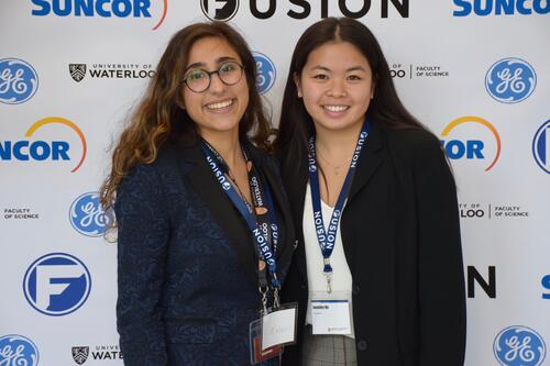 Two females smiling standing in front of Fusion confrence banner