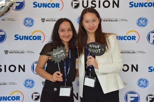 Two females smiling standing in front of Fusion confrence banner