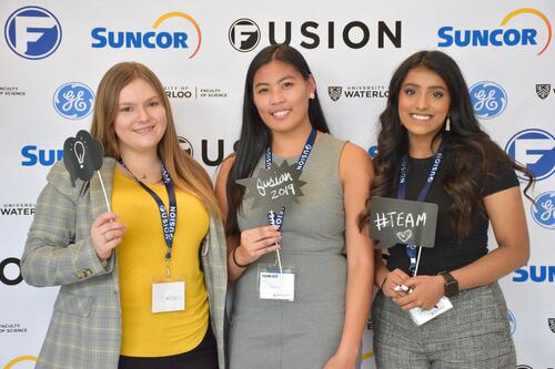 Three females standing in front of Fusion confrence banner