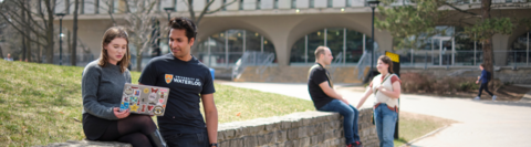 An outdoor scene on campus with two students interacting in the foreground and two interacting in the background