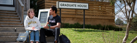 Two students sit on the steps of the Graduate House