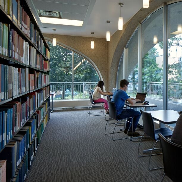 Interior of Dana Porter Library showing bookshelves and students studying at desks with laptops.