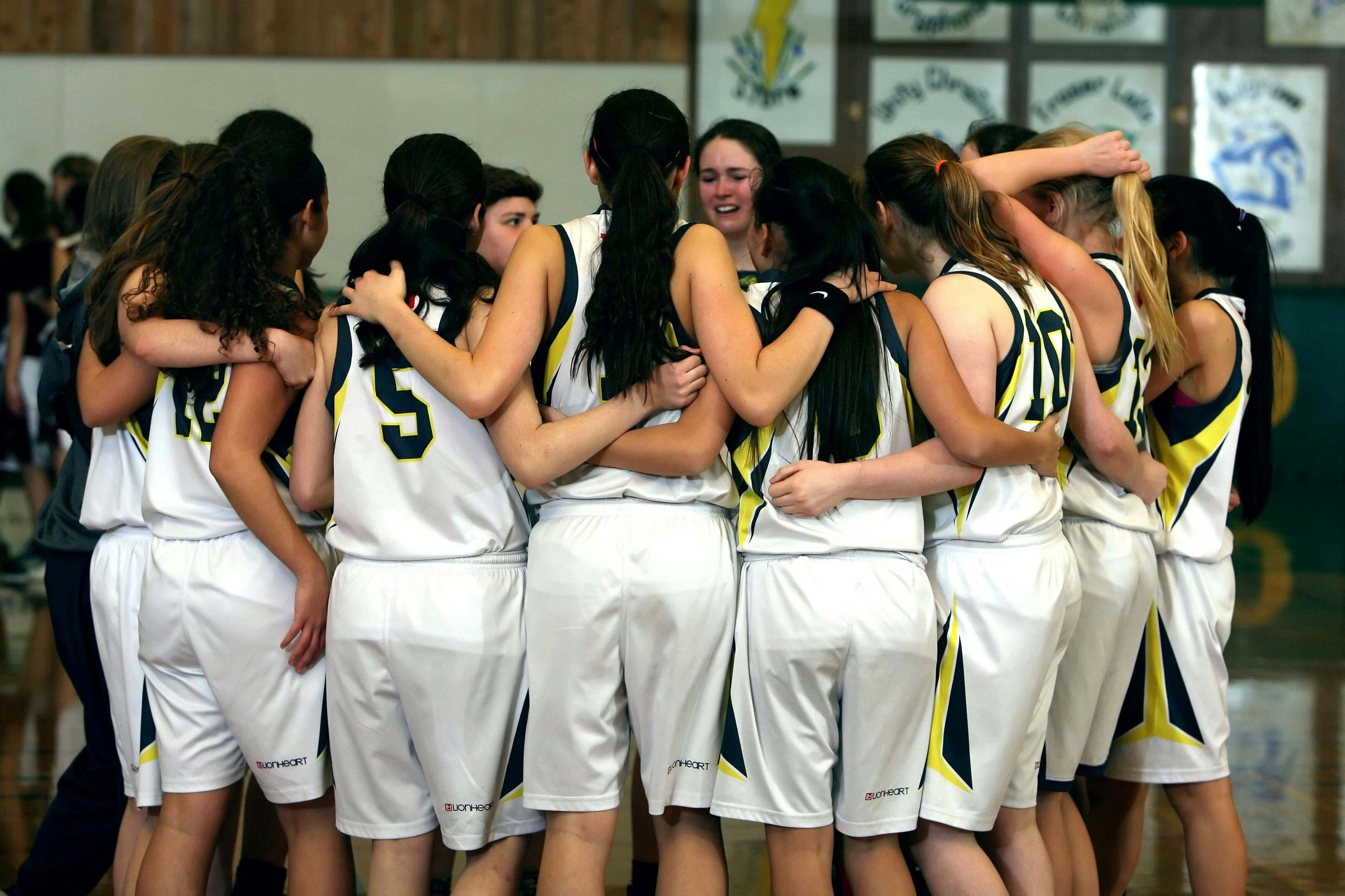 A group of female basketball players standing in a huddle with white, yellow, and black uniforms on.