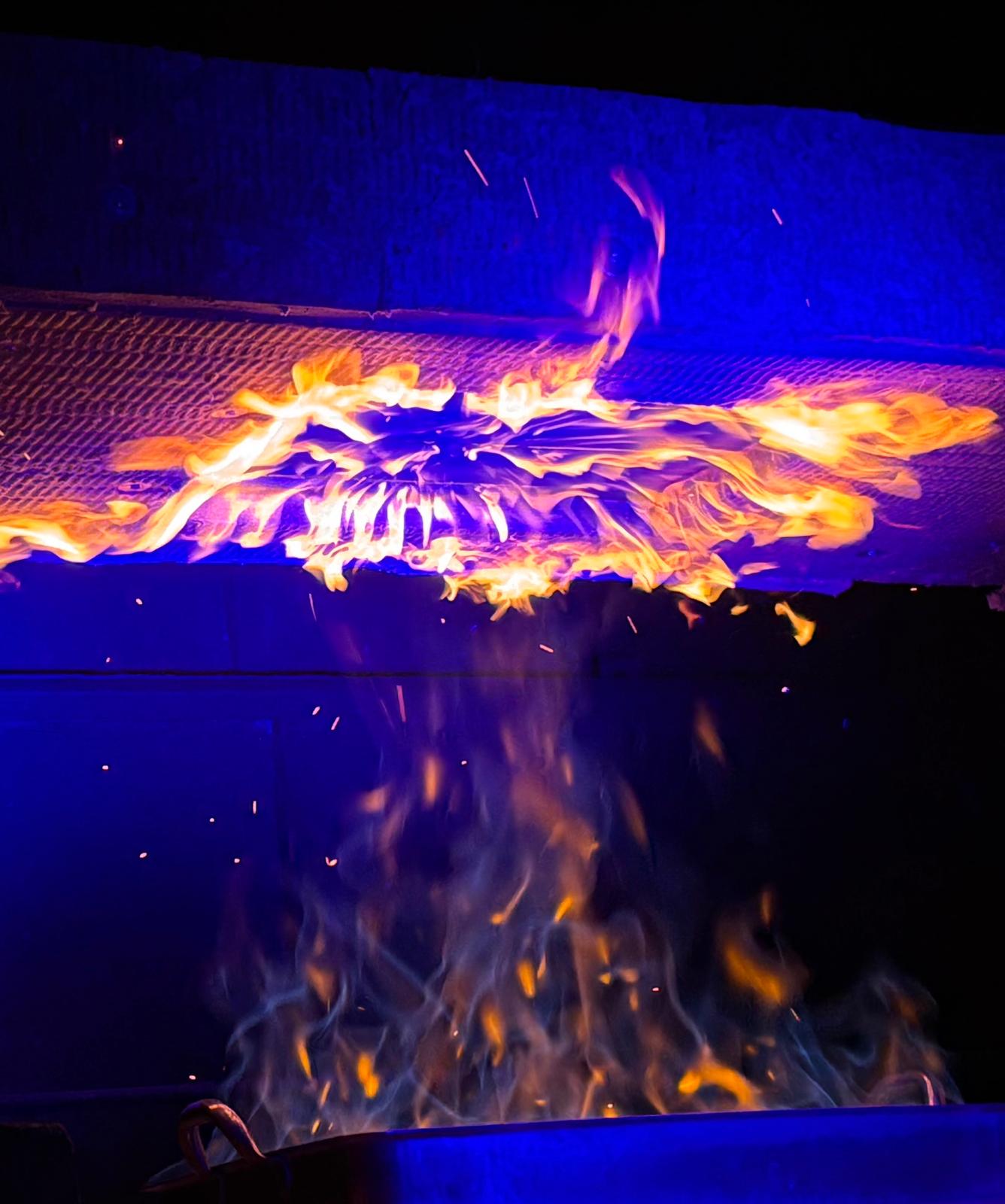 Flames crawling along a grated surface, surrounded by blue lighting.