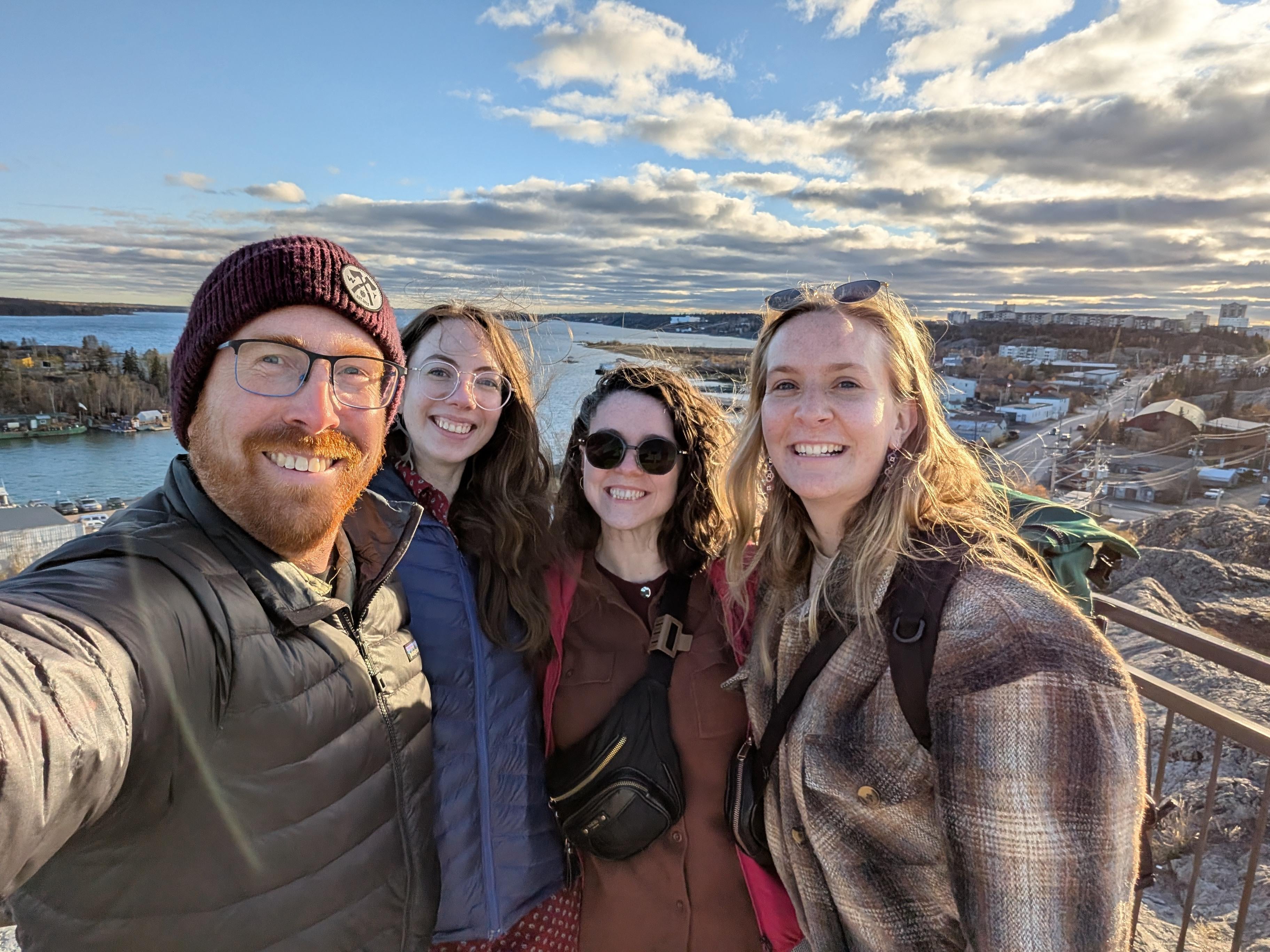 Four researchers standing on top of a hill/mountain with a river and a city in the background