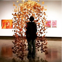 student at art exhibit looking at artwork featuring orange leafs hanging from ceiling, appearing as if they were thrown into the air