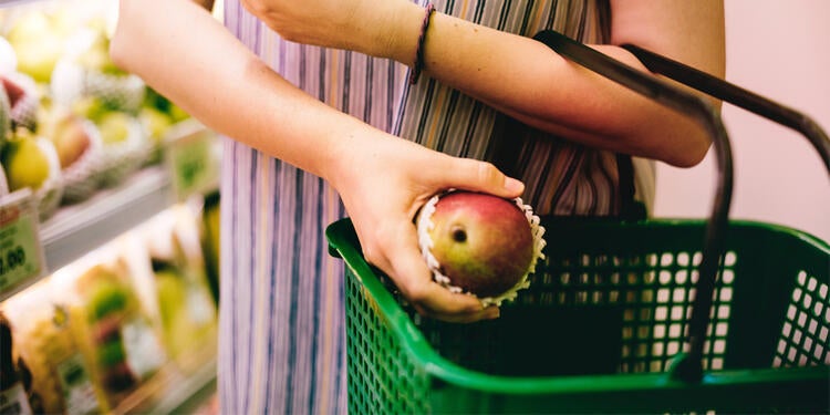 Girl putting fruit in a grocery basket showing one way how to save money as a student