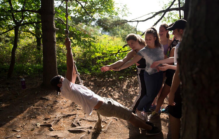 A group of students catch one of their group mates as he swings over an obstable.