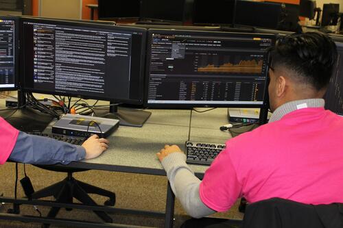a student in a pink faculty of math shirt analyzing data and research on a computer