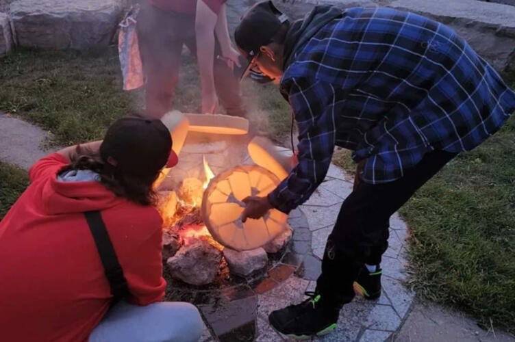 3 people holding drums over a fire
