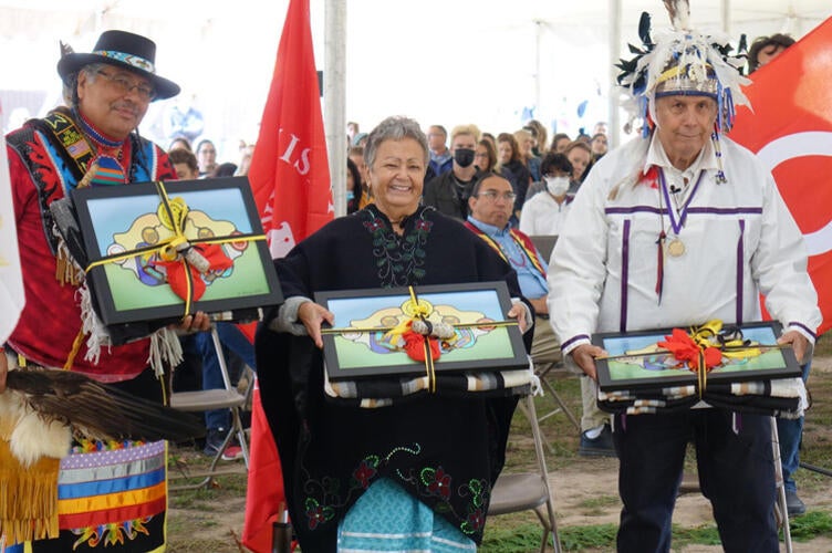 Three Elders and Knowledge Keepers hold gifts while looking toward the camera.