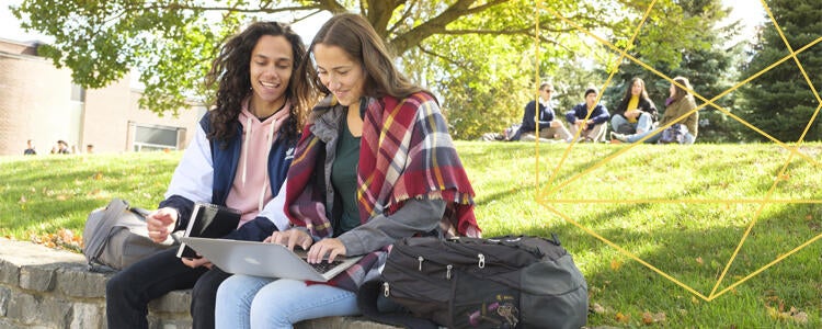 Two students sitting on grassy hill with a laptop at the University of Waterloo