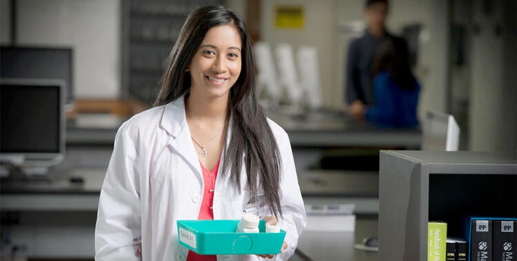 A student in Waterloo's pharmacy degree program holds a tray of pills while wearing a white lab coat.