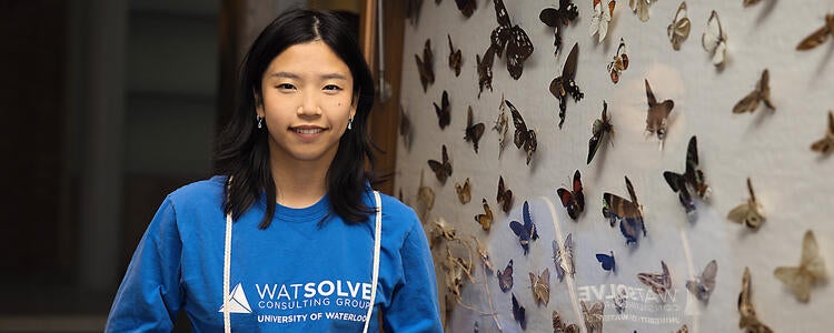 A student in a blue t-shirt stands beside a display of butterflies at the University of Waterloo.