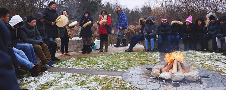 a group of people playing frame drums and sitting around a ceremonial fire