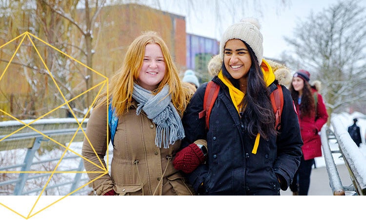 Students in winter coats and hats walk across a bridge