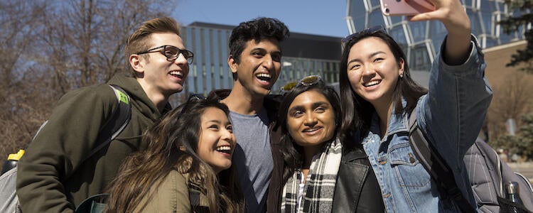 a group of five students smiling and taking a photo of themselves