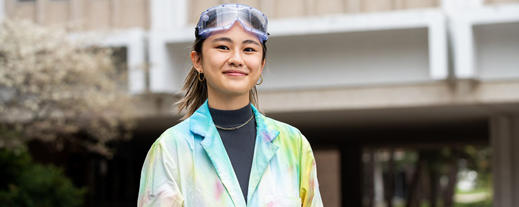 an Honours Science student wearing a tie-dye lab coat and goggles smiling