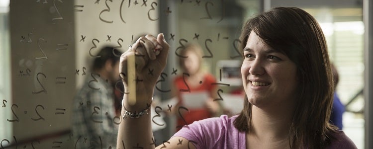 Female student writing equation on whiteboard