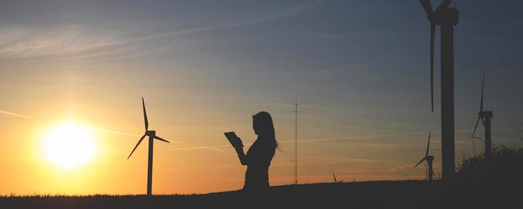 Person silhouetted with wind turbines and setting sun in the background