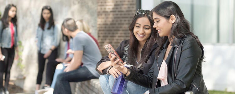 Two students sitting outside looking at something on their phone