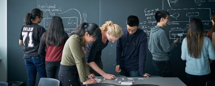 Systems Design Engineering students work together on a problem on a chalkboard