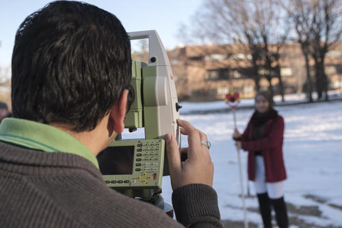 Aujas and a classmate use surveying equipment outdoors on a winter day