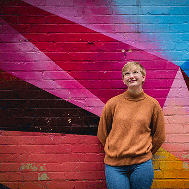 Abby stands in front of a brightly painted mural