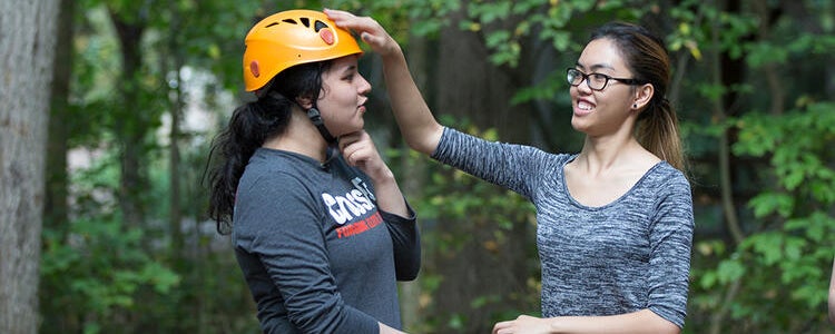 A Recreation student adjusting her classmate's helmet on a first-year class retreat
