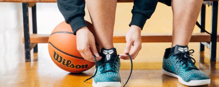 Close up of student tying shoelaces with basketball beside him