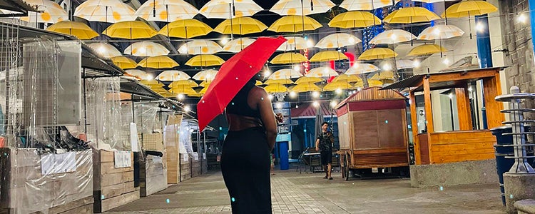 Akua standing under a red umbrella