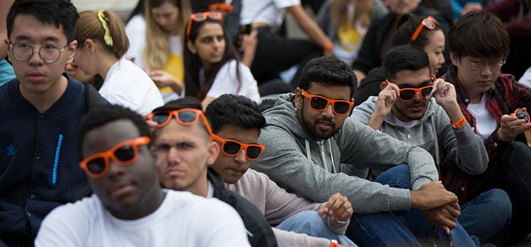 Students in orange Arts sunglasses sitting together outside at an event