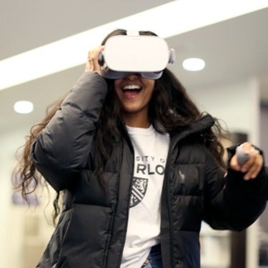 A student laughs while wearing a VR headset and manipulating her view using a handheld control
