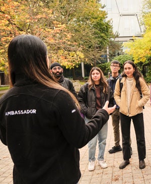 A student ambassador with her back to the camera speaks to students during a campus tour