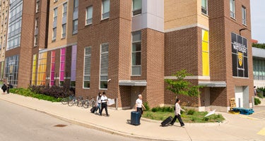 Students and their families walking infront of Claudette Millar Hall on move-in day with suitcases in hand