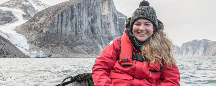 A student in Waterloo's geography degree program sits in a boat in the Arctic while wearing a bright red coat. 