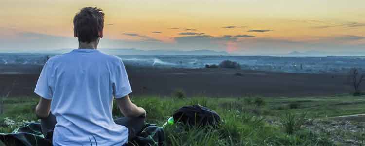 student meditating on top of hill with sunset in the horizon