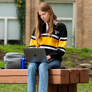 Student sitting outside on bench using a laptop