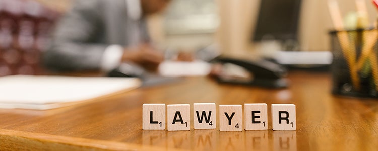  A lawyer in Canada working at their desk. Sitting on their desk are wooden block letters that spell out the word lawyer.