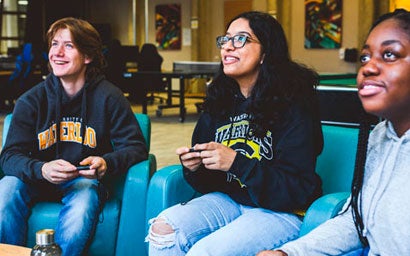 Three students playing video games together in a residence common space