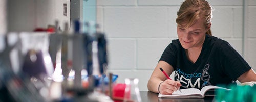 Math student in a lab writing in a notebook