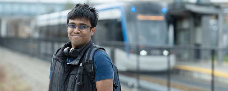 student smiling at camera with LRT bus behind him