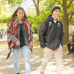 Two students wearing jackets on a tree-lined walkway