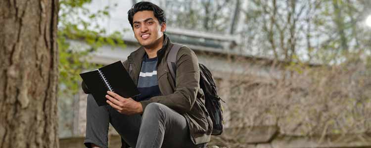 student sitting on bench with book in hand