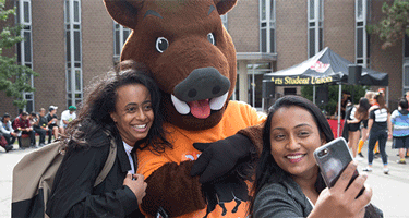 Two students talking a selfie with a boar mascot